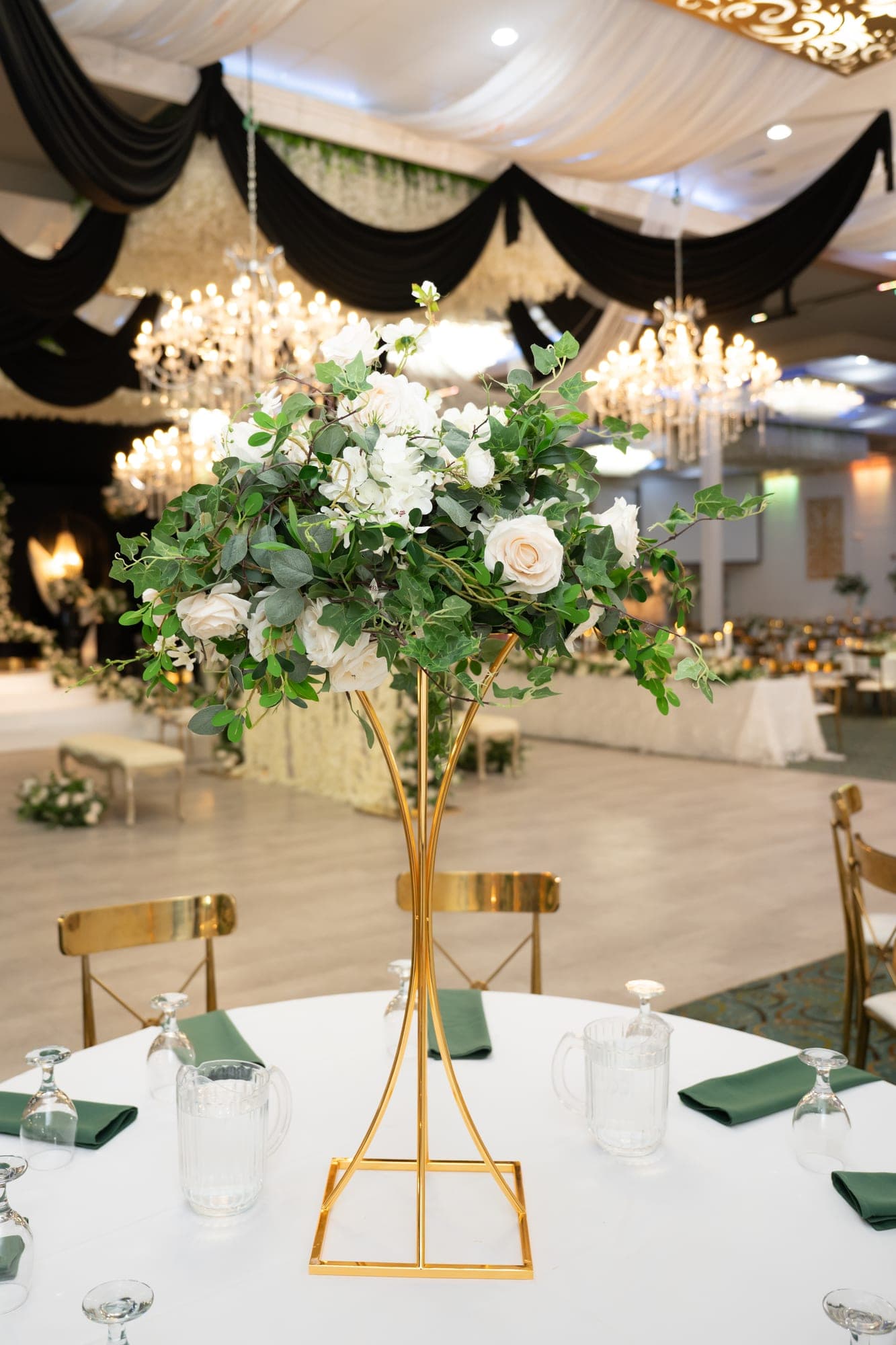A tall arrangement of ivory roses and greenery on a reception table beneath chandeliers